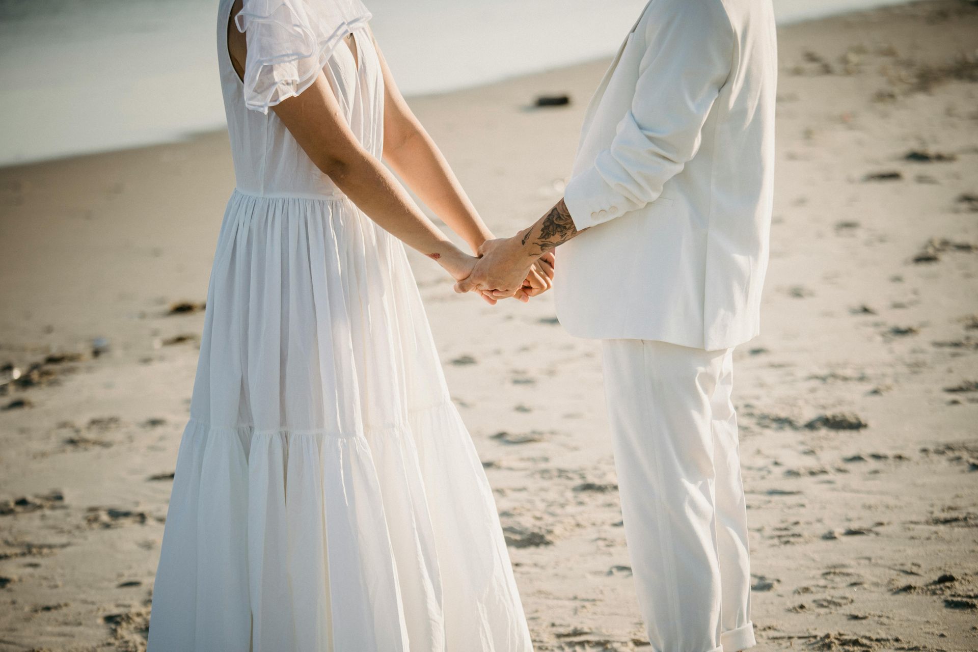 Couple holding hands on the beach in white wedding attire