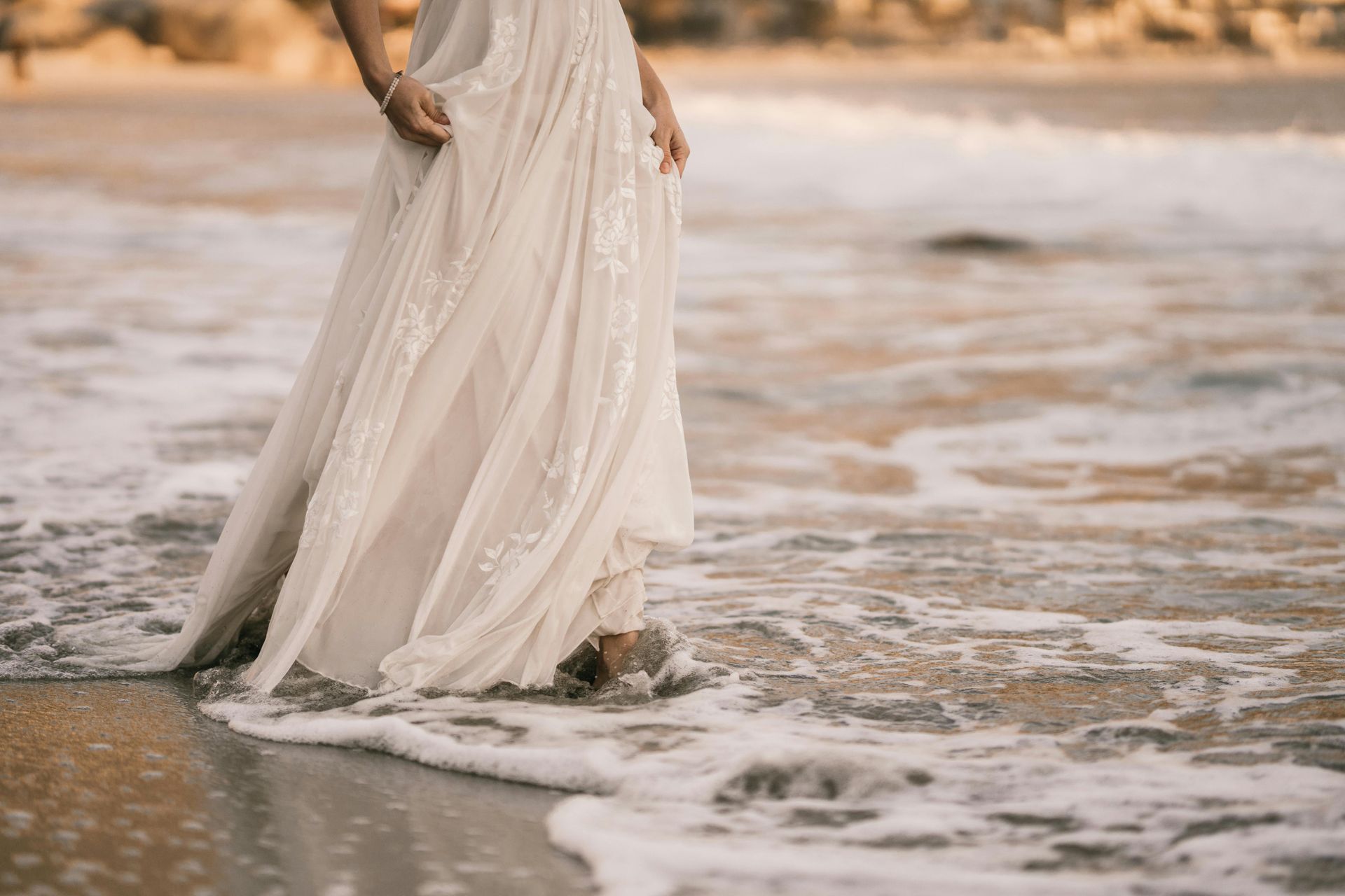Bride walking through the ocean waves in a flowing dress at golden hour