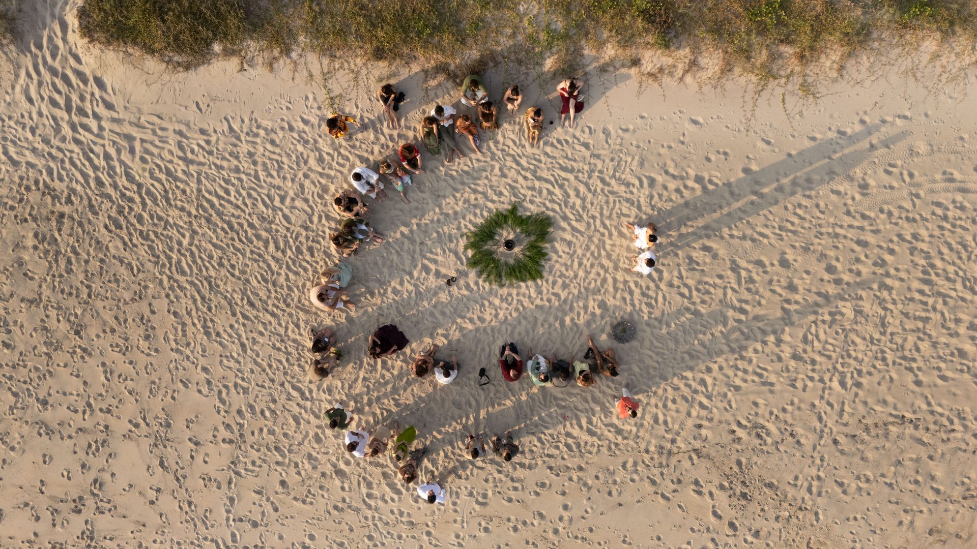 Aerial view of beach wedding ceremony with guests seated in V-shape on sand