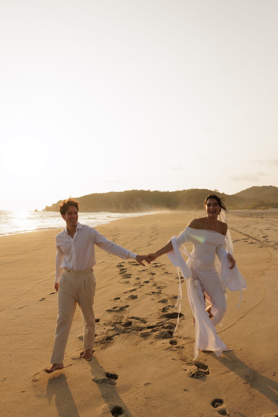 Bride and groom holding hands on beach at golden hour in Puerto Escondido
