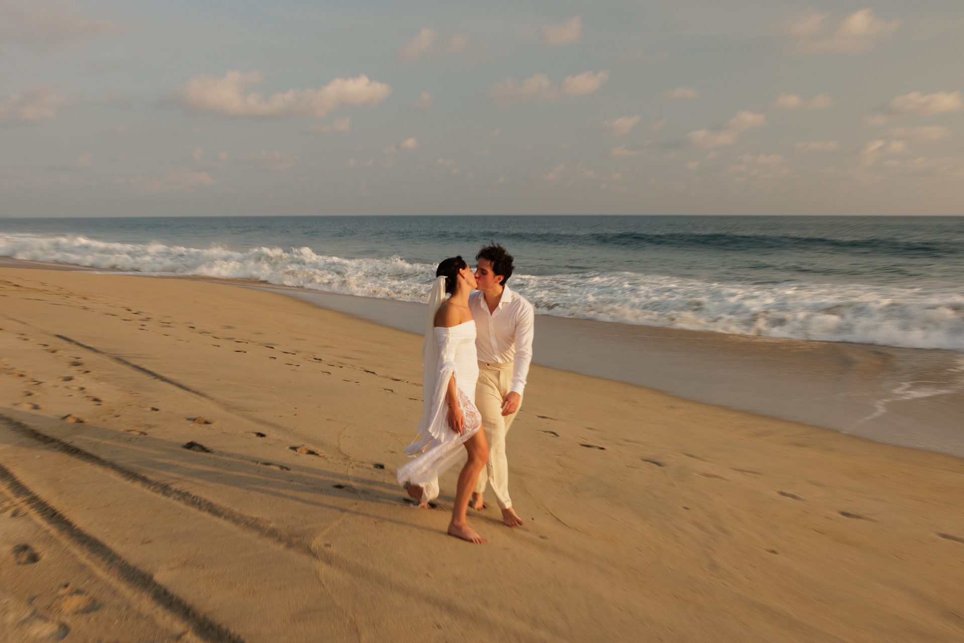 Couple sharing a kiss on the beach with Pacific waves behind them