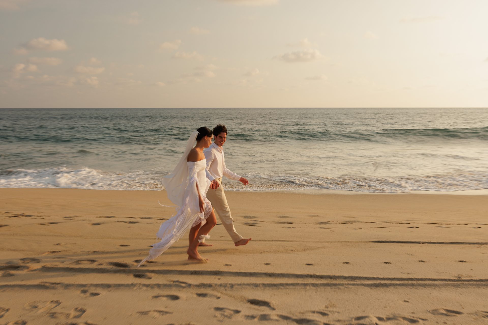 Newlyweds running joyfully along the beach at sunset