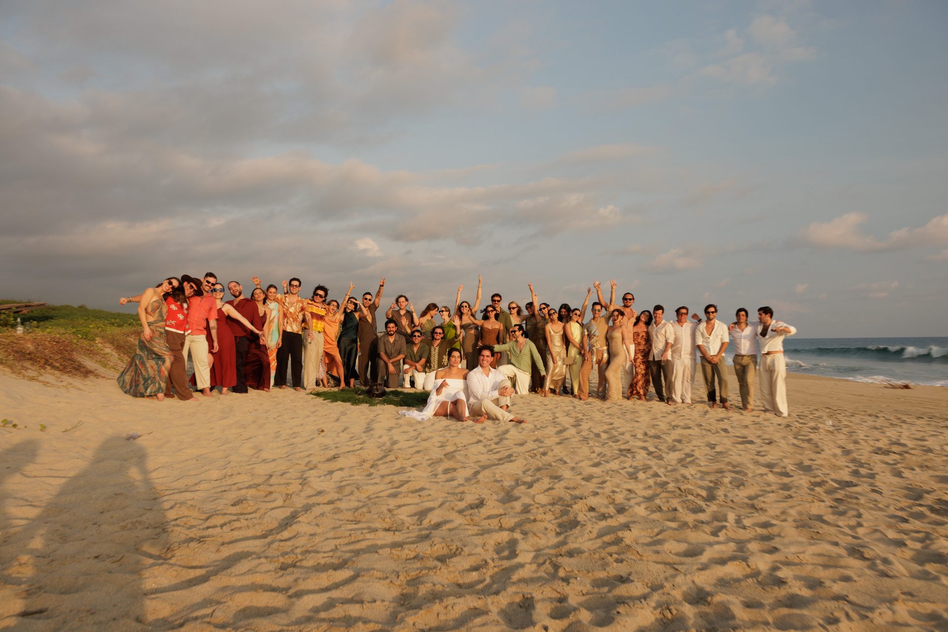 Full wedding group photo on beach at golden hour