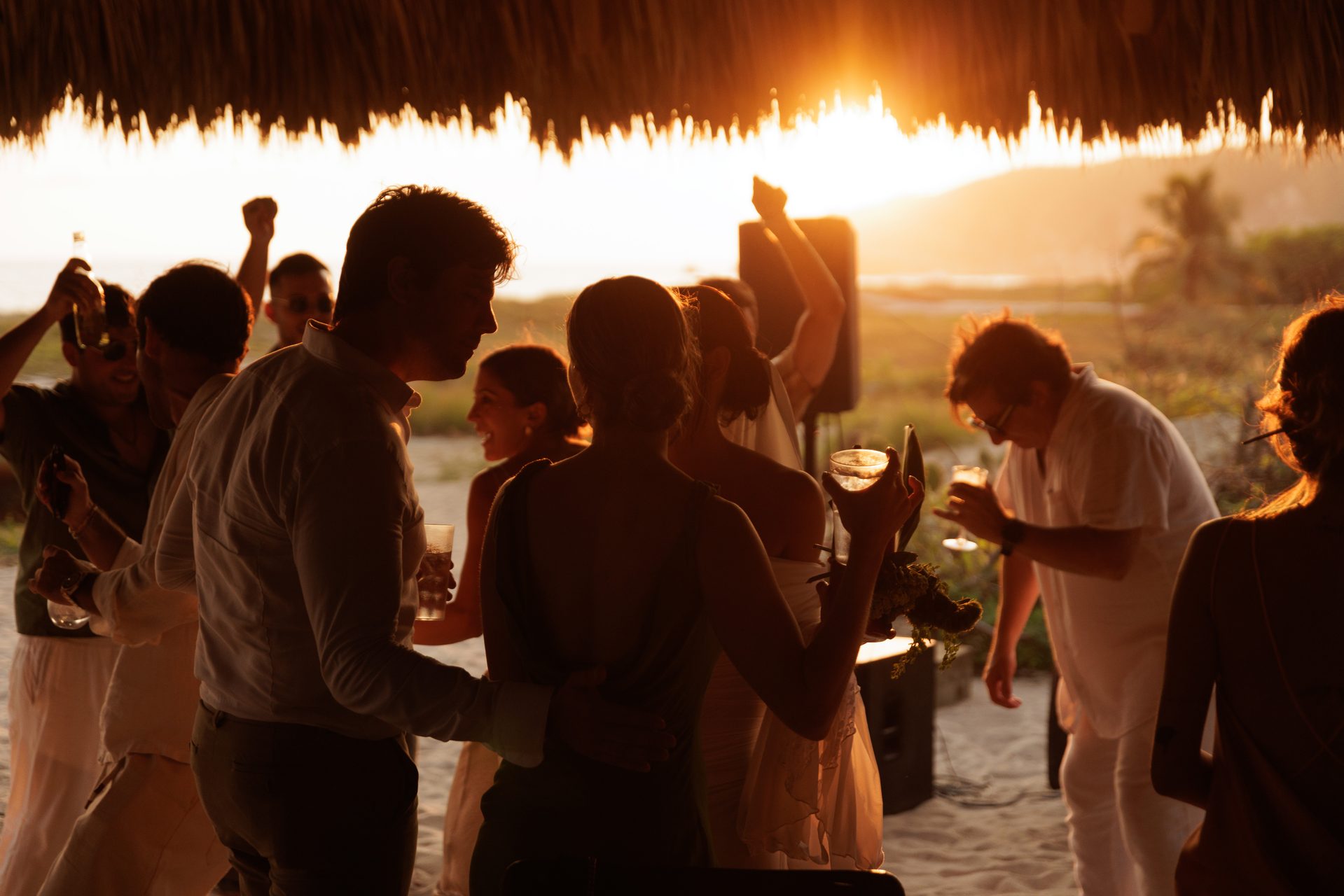 Wedding guests dancing at golden hour under palapa
