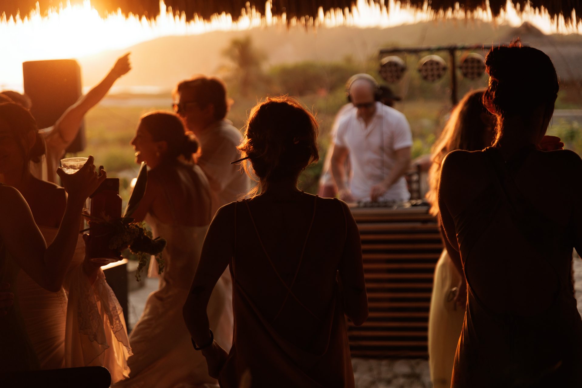 Wedding guests silhouetted against golden sunset at beach reception