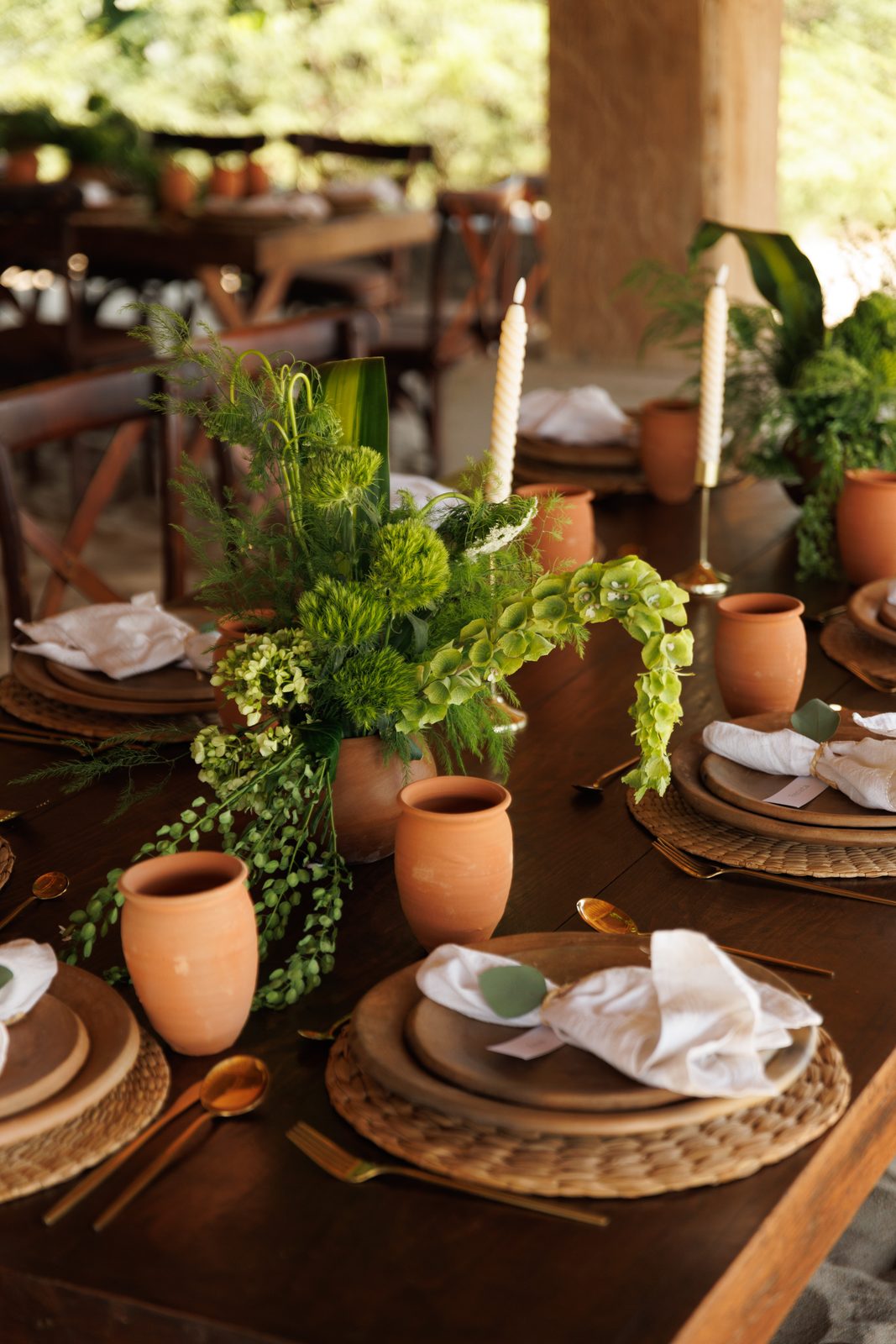 Rustic wedding table setting with terracotta cups and tropical greenery